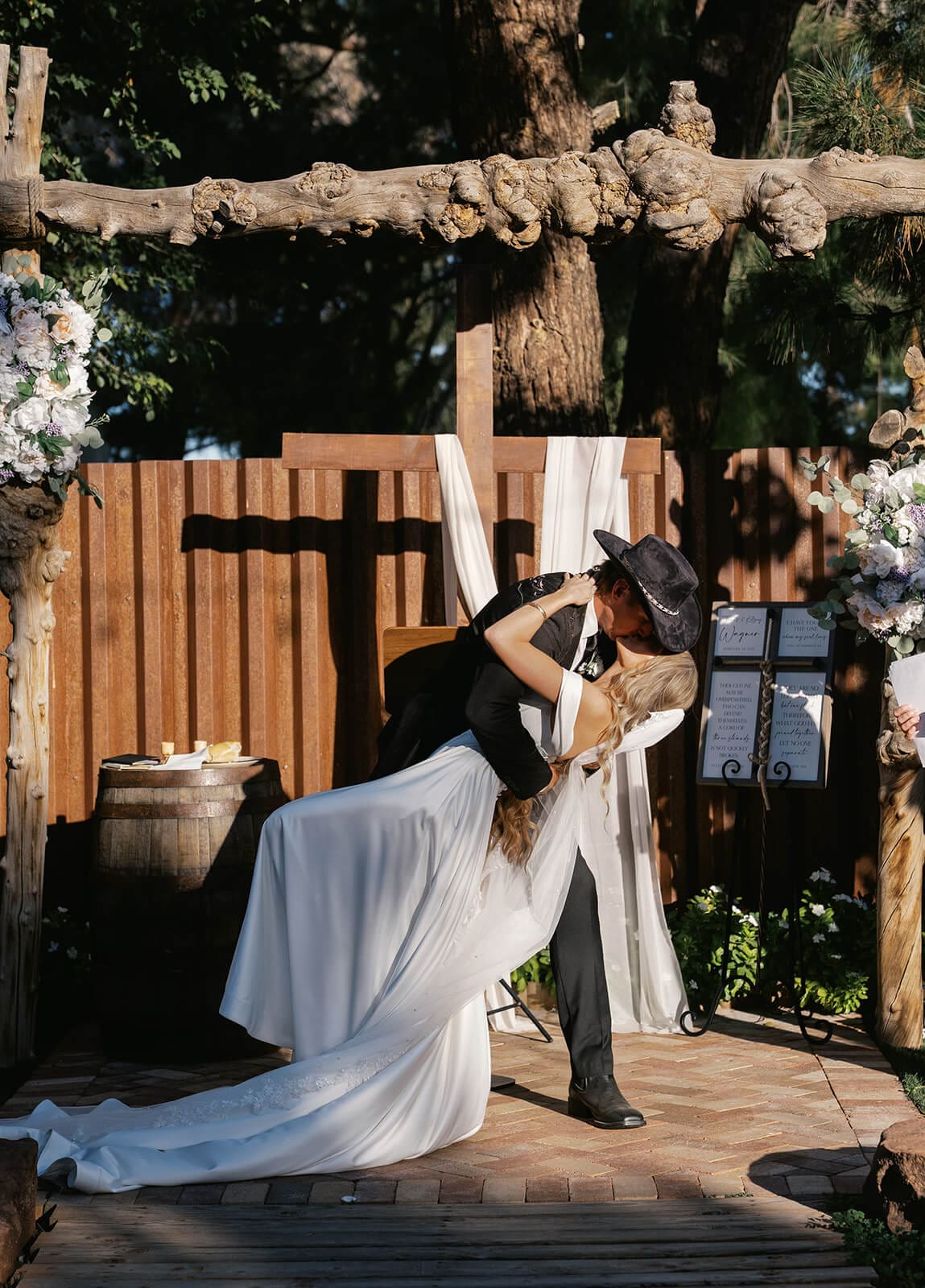 Groom in a cowboy hat dipping and kissing his bride during portraits at Knotty Barn, a rustic garden wedding venue in Queen Creek Arizona
