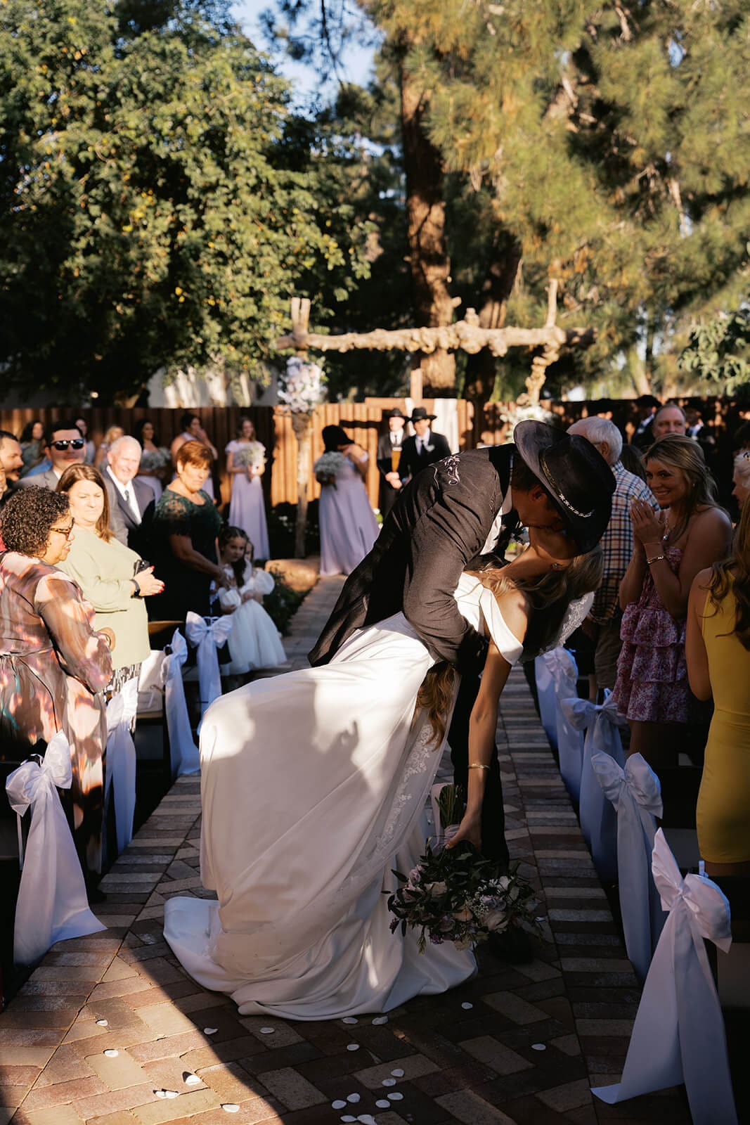Bride walking down a brick aisle lined with guests and soft blue sashes at Knotty Barn, a rustic garden wedding venue in Queen Creek Arizona