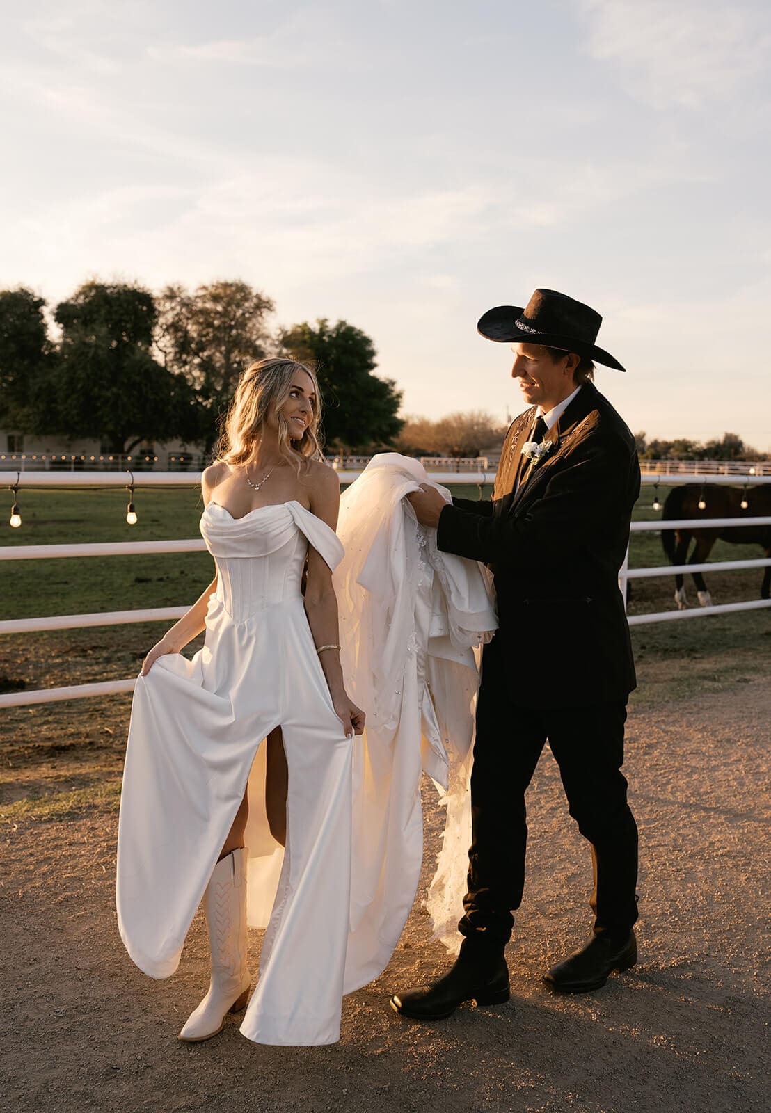 Bride and groom laughing together at golden hour near a fence line at Knotty Barn, a rustic wedding venue in Queen Creek Arizona
