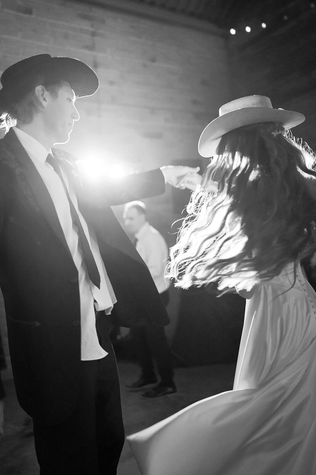 Black and white photo of bride in a wide brim hat spinning on the dance floor at Knotty Barn wedding venue in Queen Creek Arizona
