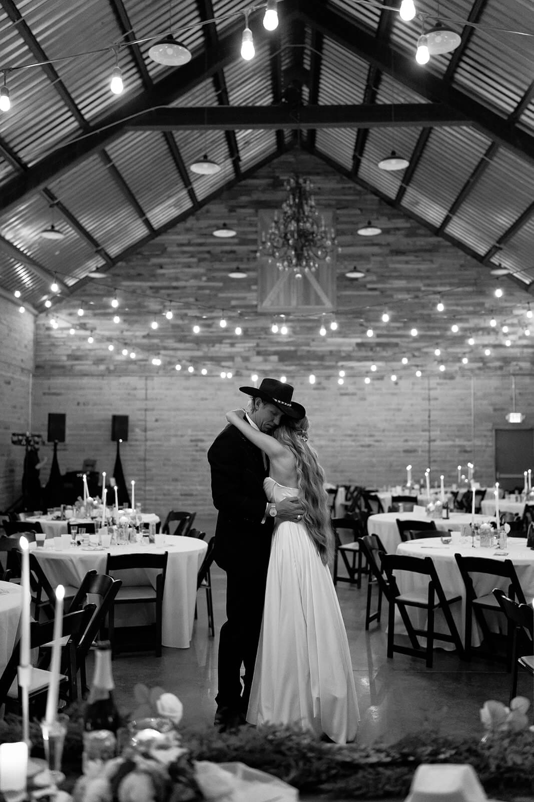 Black and white photo of bride and groom embracing on the dance floor inside the historic barn at Knotty Barn wedding venue in Queen Creek Arizona
