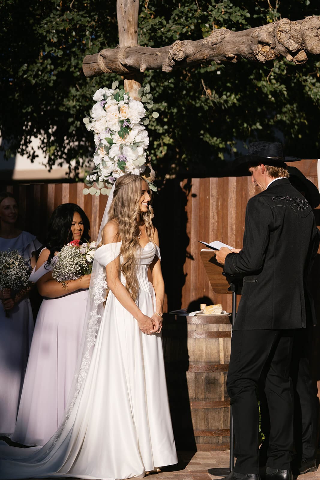 Groom reading his vows to his bride under a wood and floral arch at Knotty Barn wedding venue in Queen Creek Arizona
