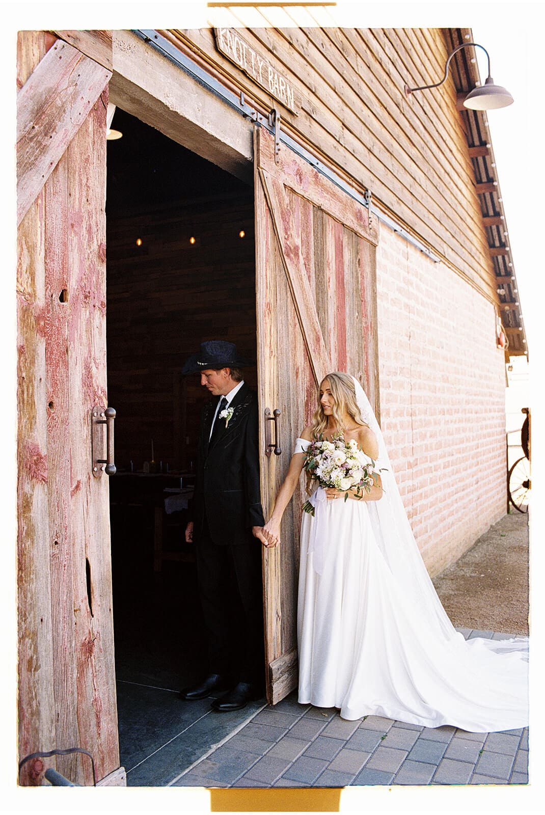 Bride and groom standing on either side of the rustic wooden barn doors at Knotty Barn, a garden wedding venue in Queen Creek Arizona