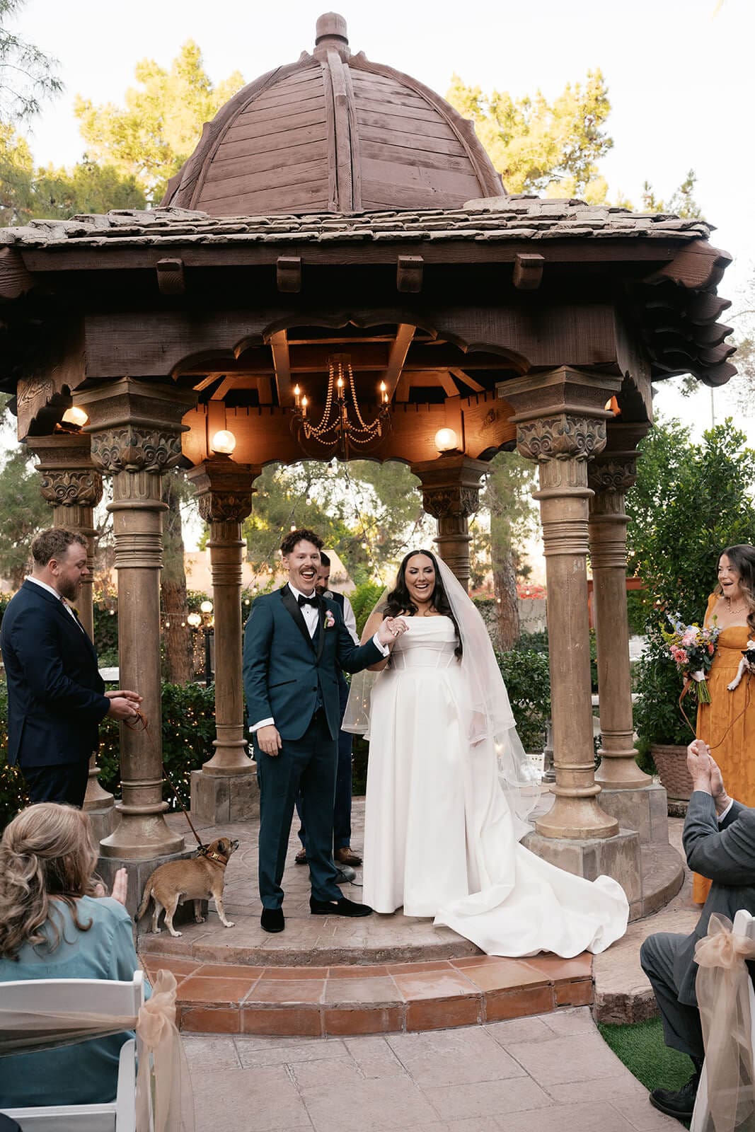 Bride and groom celebrating under the ornate gazebo with guests cheering around them at The Wright House garden wedding venue in Mesa Arizona

