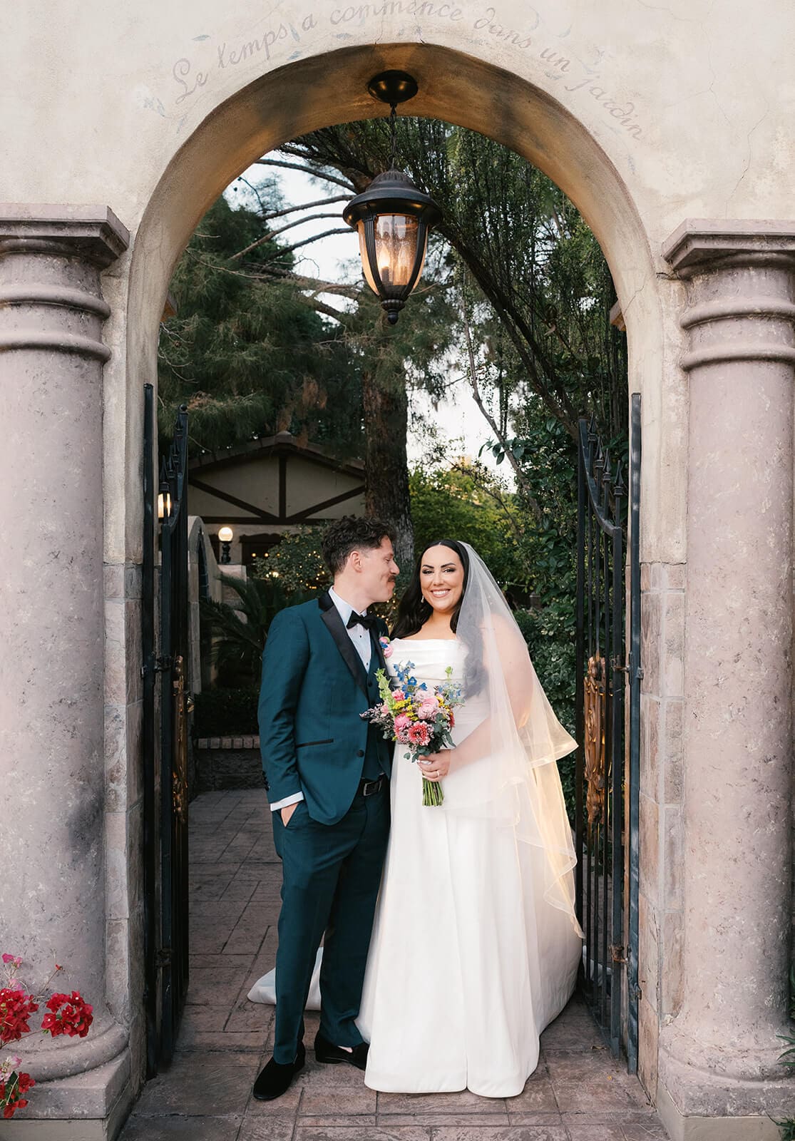 Bride and groom sharing a quiet moment together framed by stone archway gates at The Wright House, a garden wedding venue in Mesa Arizona
