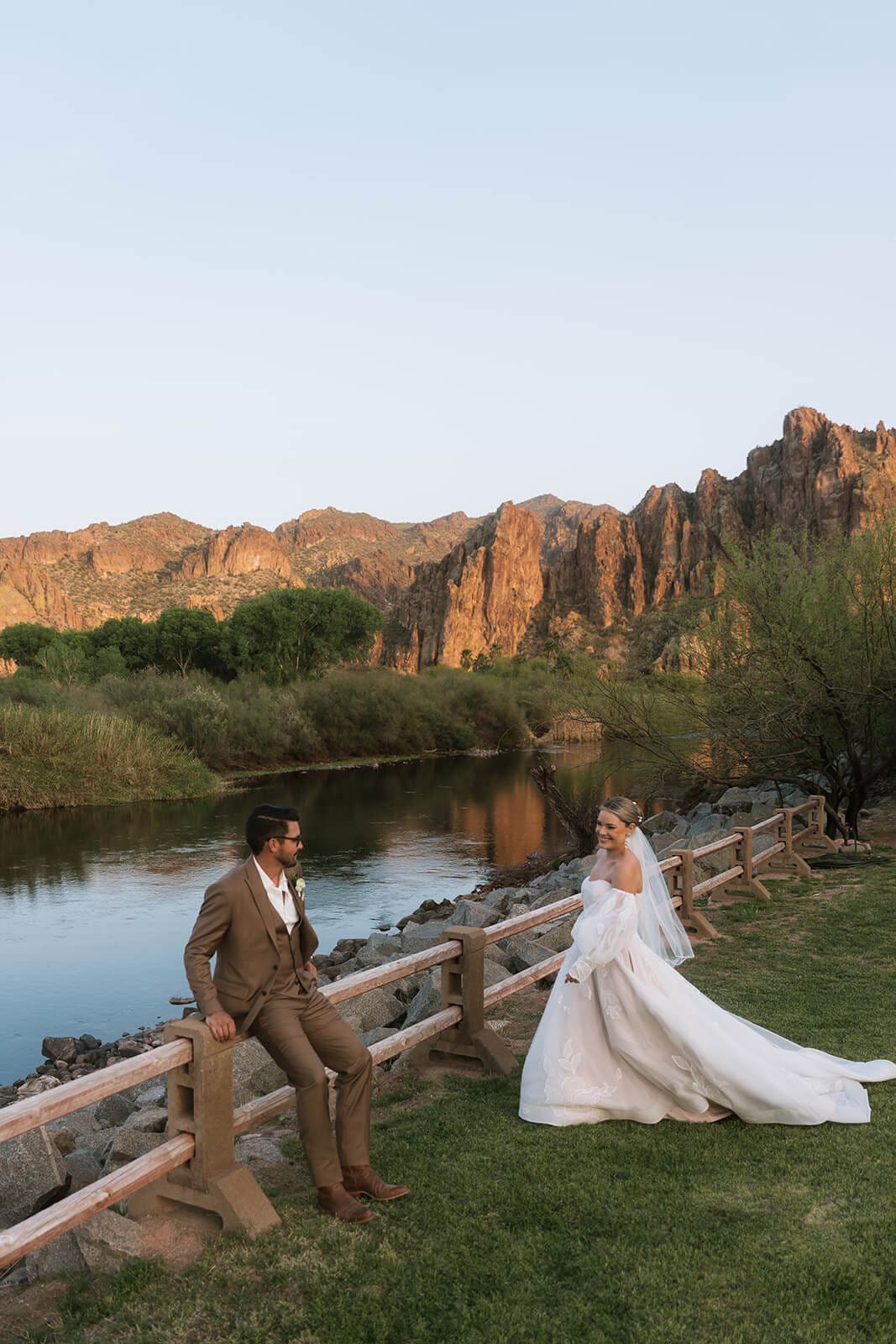 Bride and groom standing on a wooden bridge facing each other with the Salt River and Bulldog Cliffs behind them at Saguaro Lake Guest Ranch wedding venue in Mesa Arizona
