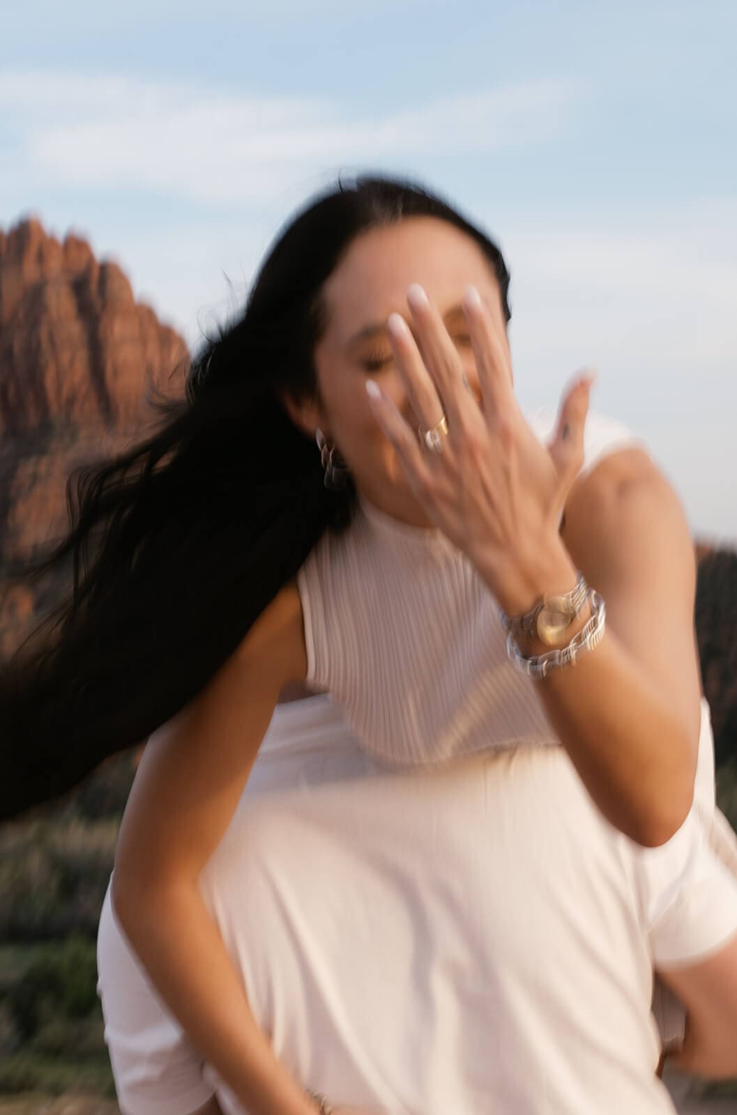A woman laughs and covers her face with her hand while a man stands beside her, with Sedona's red rock formations softly blurred in the background.