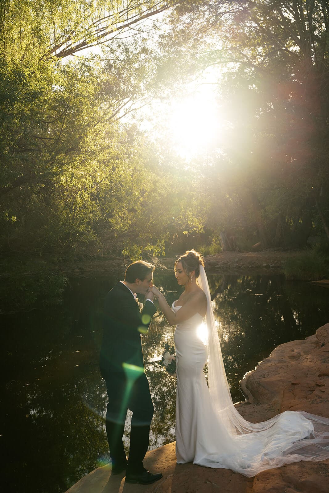 Bride and groom standing together in glowing sunlight by the creek during romantic elopement portraits after their ceremony.