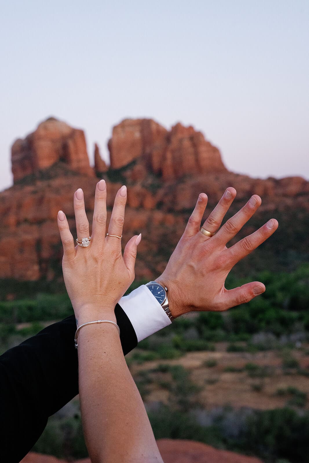 Newlyweds holding up their hands to show their wedding rings after their Sedona elopement, with Cathedral Rock softly blurred in the background.