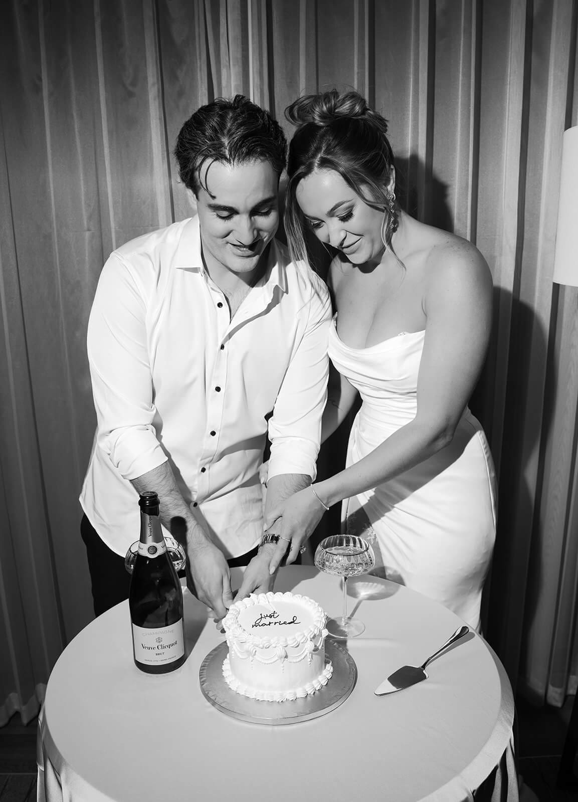 Black and white photo of newlyweds cutting their cake together during a small indoor celebration after their elopement.