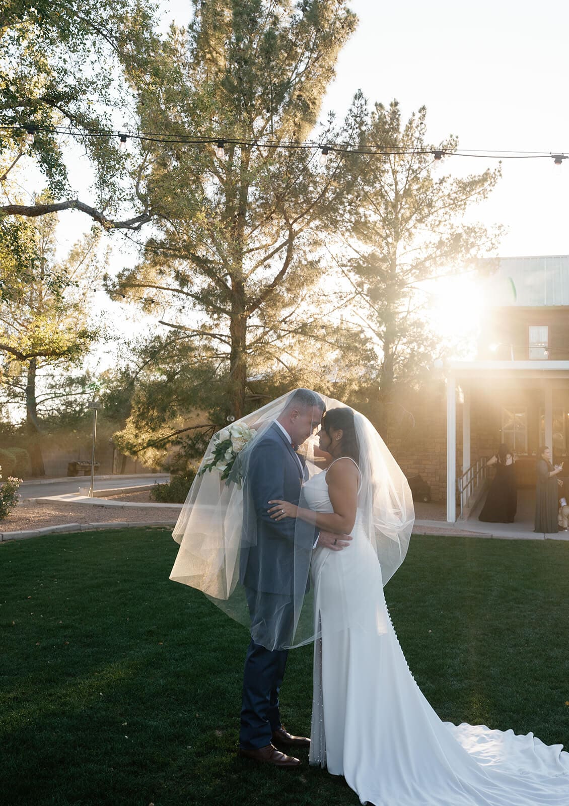 Bride and groom standing close together under a flowing veil in golden backlit sunlight at Shenandoah Mill wedding venue in Gilbert Arizona

