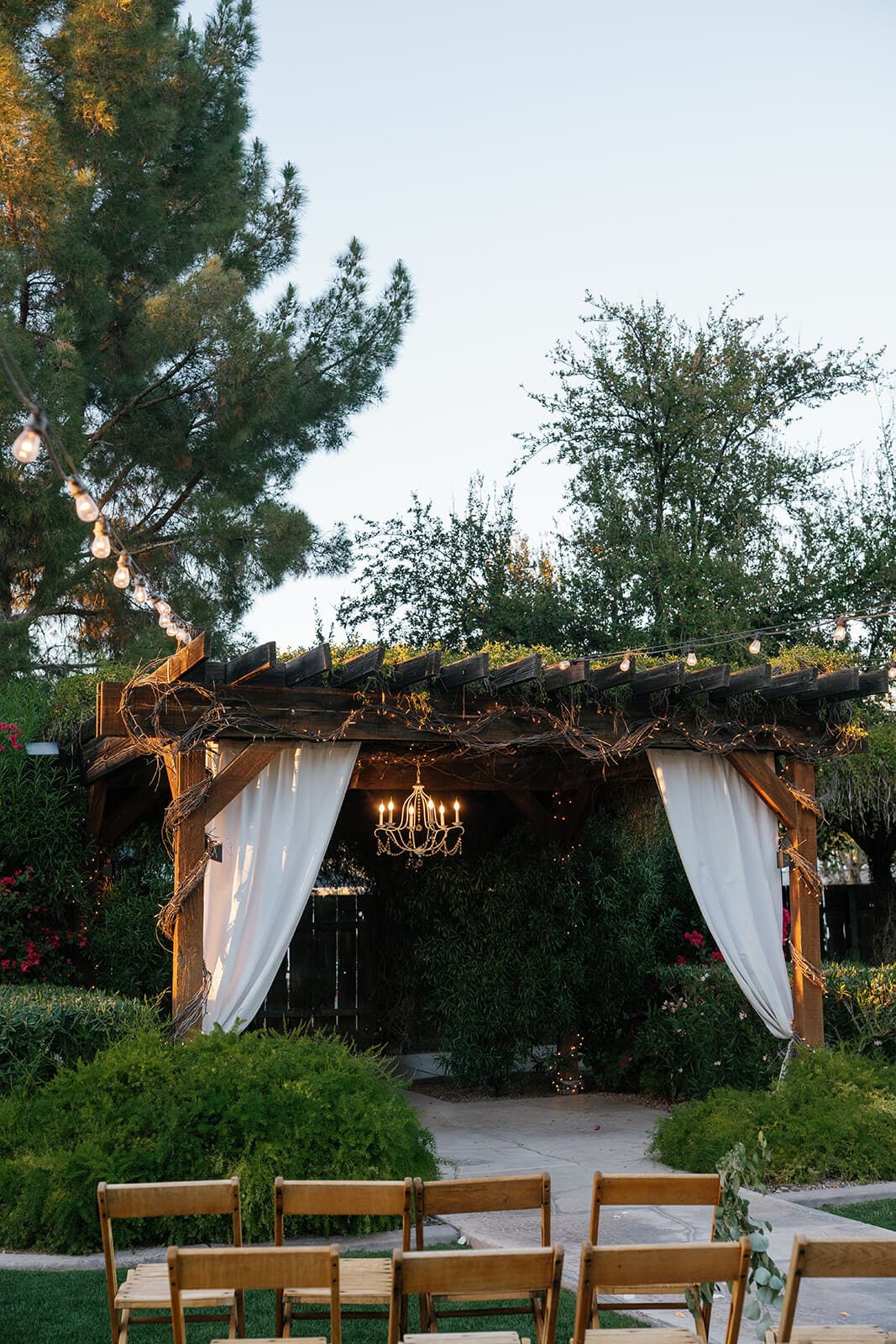 Empty draped pergola ceremony space with wooden chairs set up in the garden at Shenandoah Mill wedding venue in Gilbert Arizona
