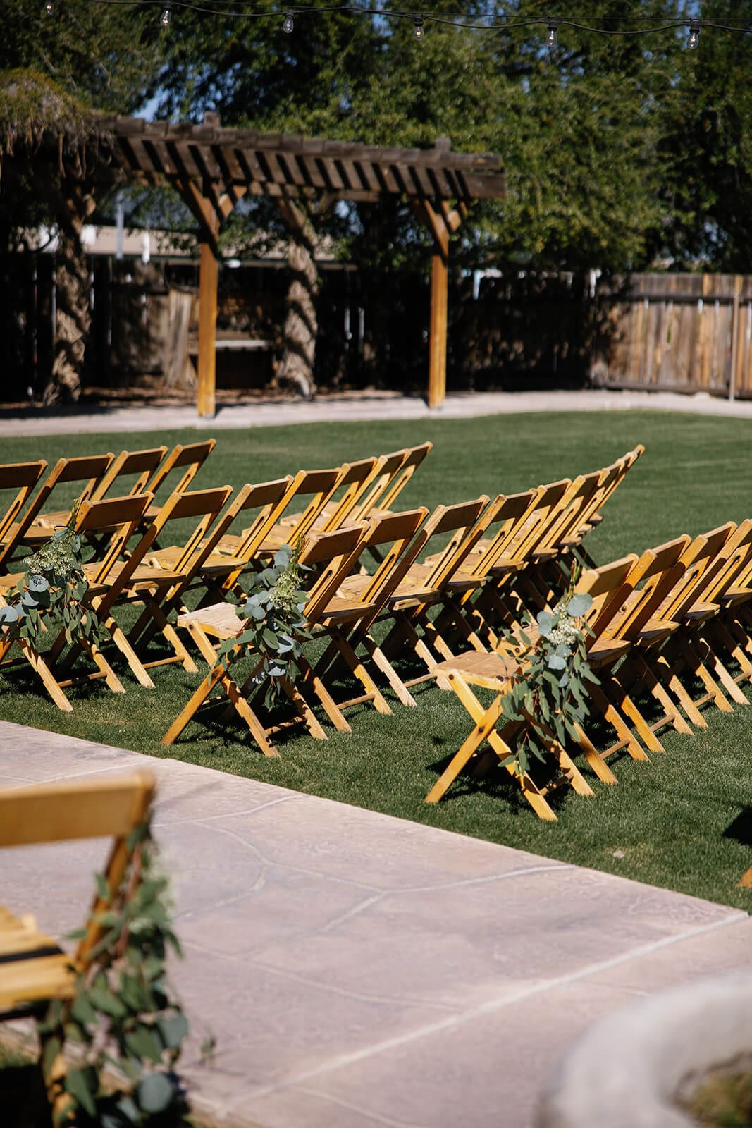Rows of wooden ceremony chairs set up on the lawn under a pergola at Shenandoah Mill garden wedding venue in Gilbert Arizona
