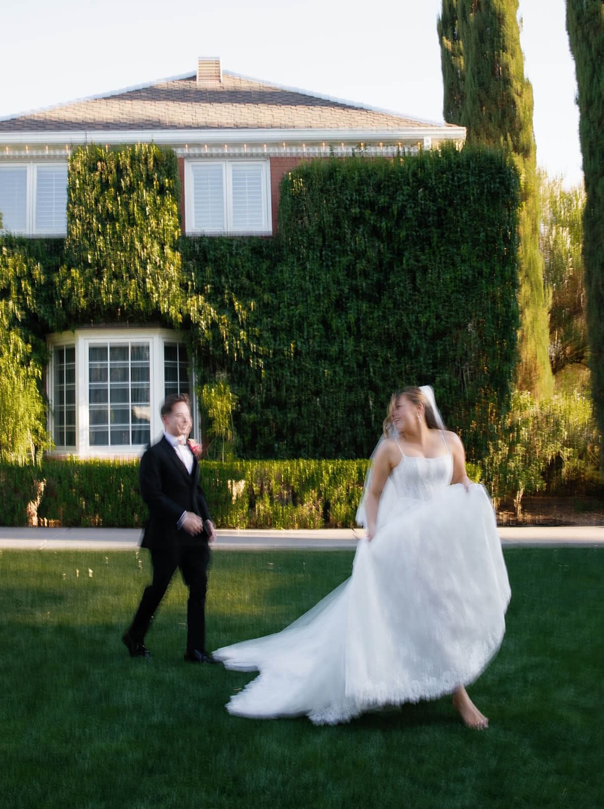 Bride twirling on the manicured lawn with her groom watching beside the ivy covered manor at Stonebridge Manor garden wedding venue in Mesa Arizona
