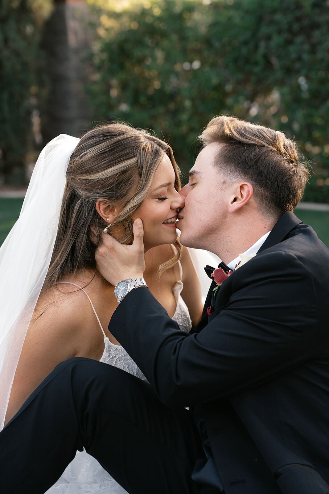 Bride and groom sharing a kiss while sitting together on the lawn during wedding portraits at Stonebridge Manor.