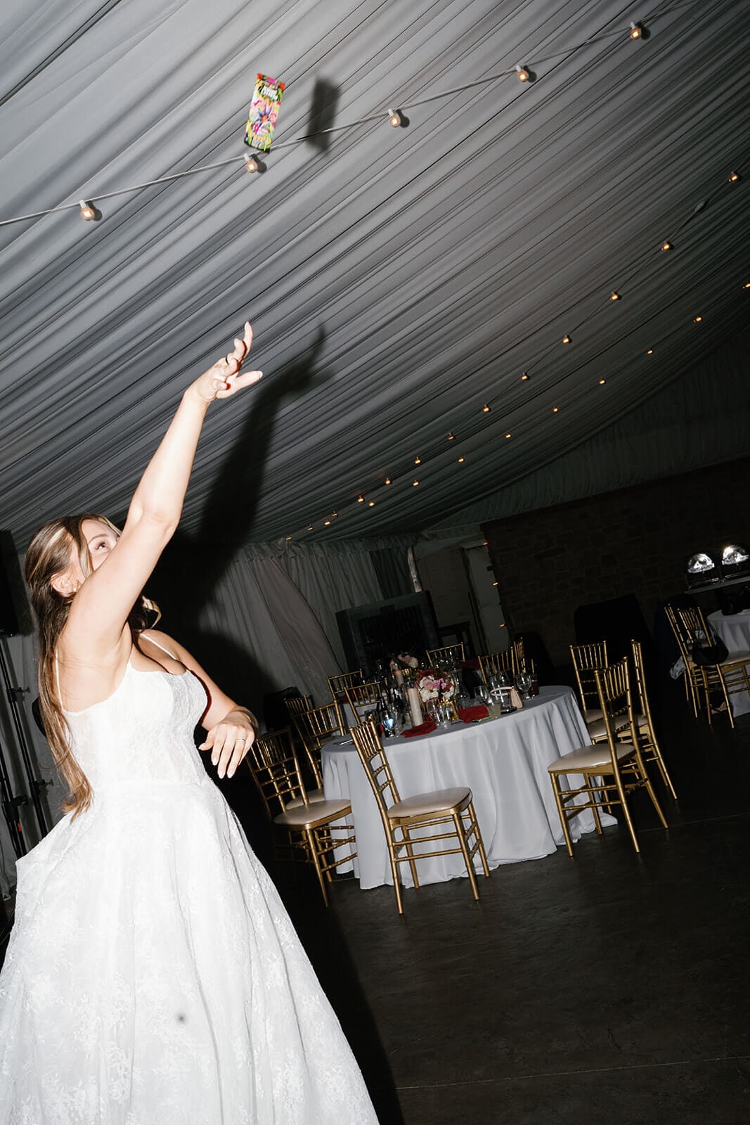 Bride tossing colorful trading card packs into the crowd during a lively reception dance floor moment inside the Stonebridge Manor reception tent.