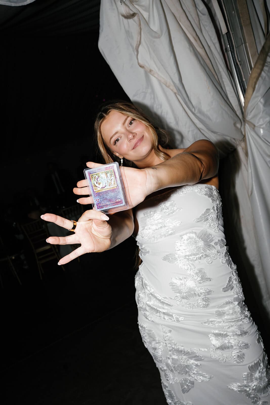 Bride holding a trading card pack toward the camera while dancing during the reception celebration at Stonebridge Manor.