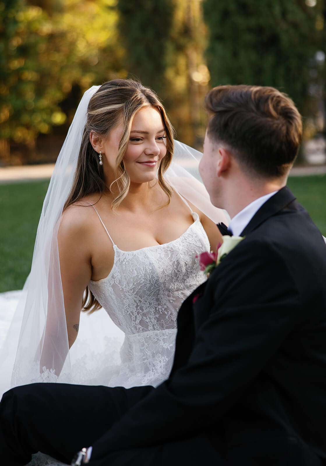 Bride and groom sitting together on the lawn during sunset portraits at Stonebridge Manor, surrounded by tall cypress trees and manicured hedges.