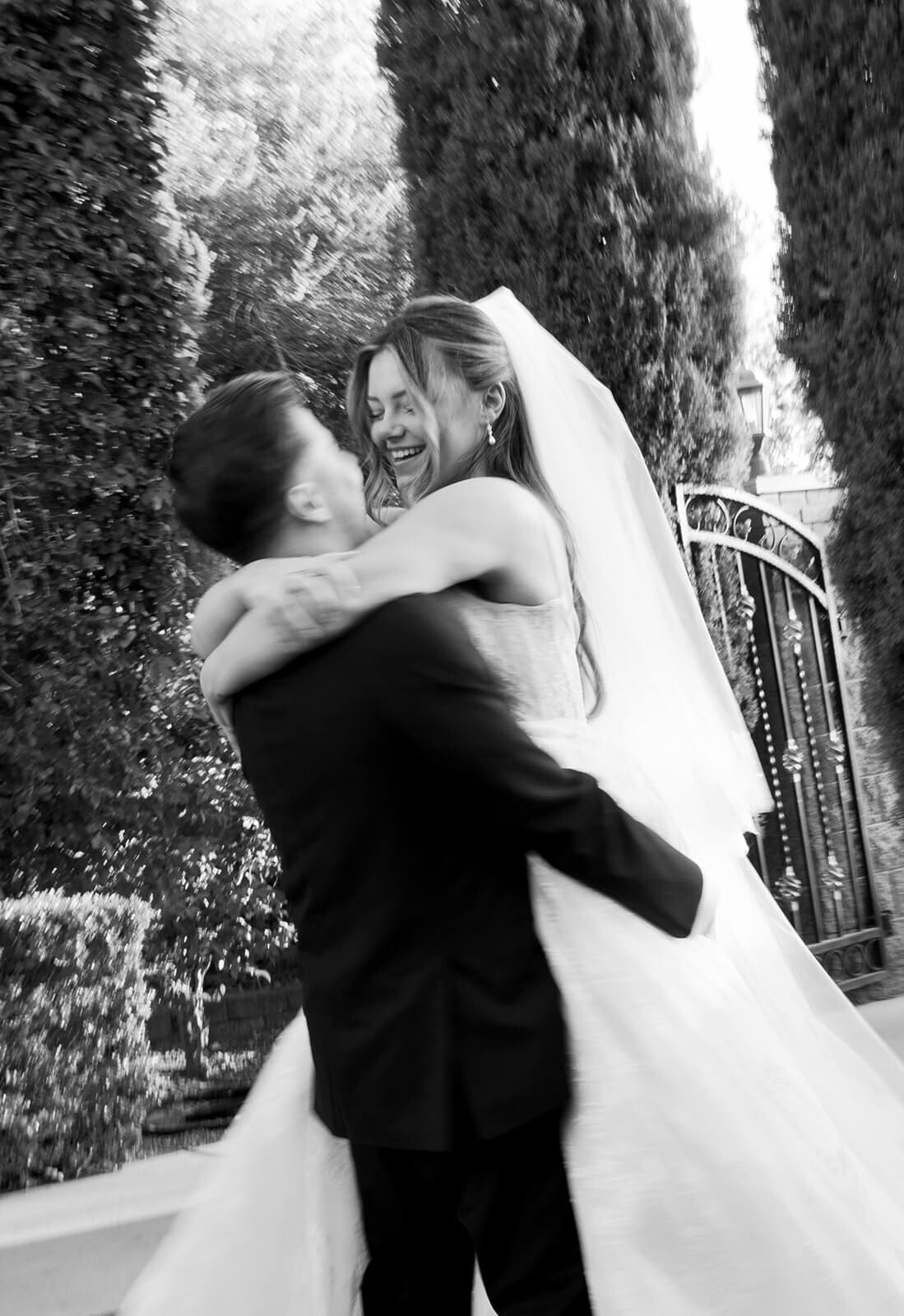 Bride jumping into the groom’s arms during wedding portraits on the Stonebridge Manor lawn, photographed in black and white.