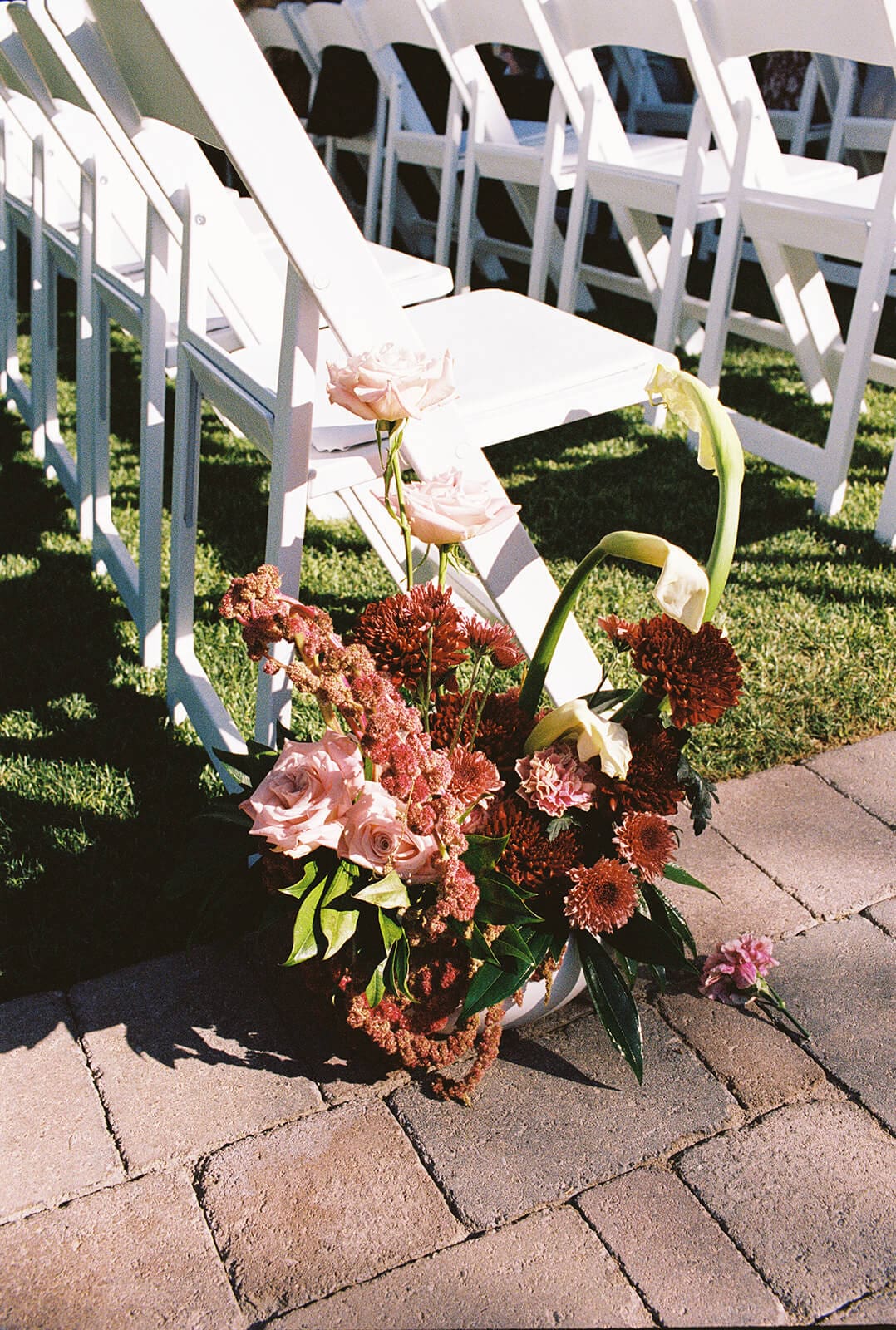 Ceremony floral arrangement with burgundy orchids and blush roses placed beside white ceremony chairs at Stonebridge Manor.
