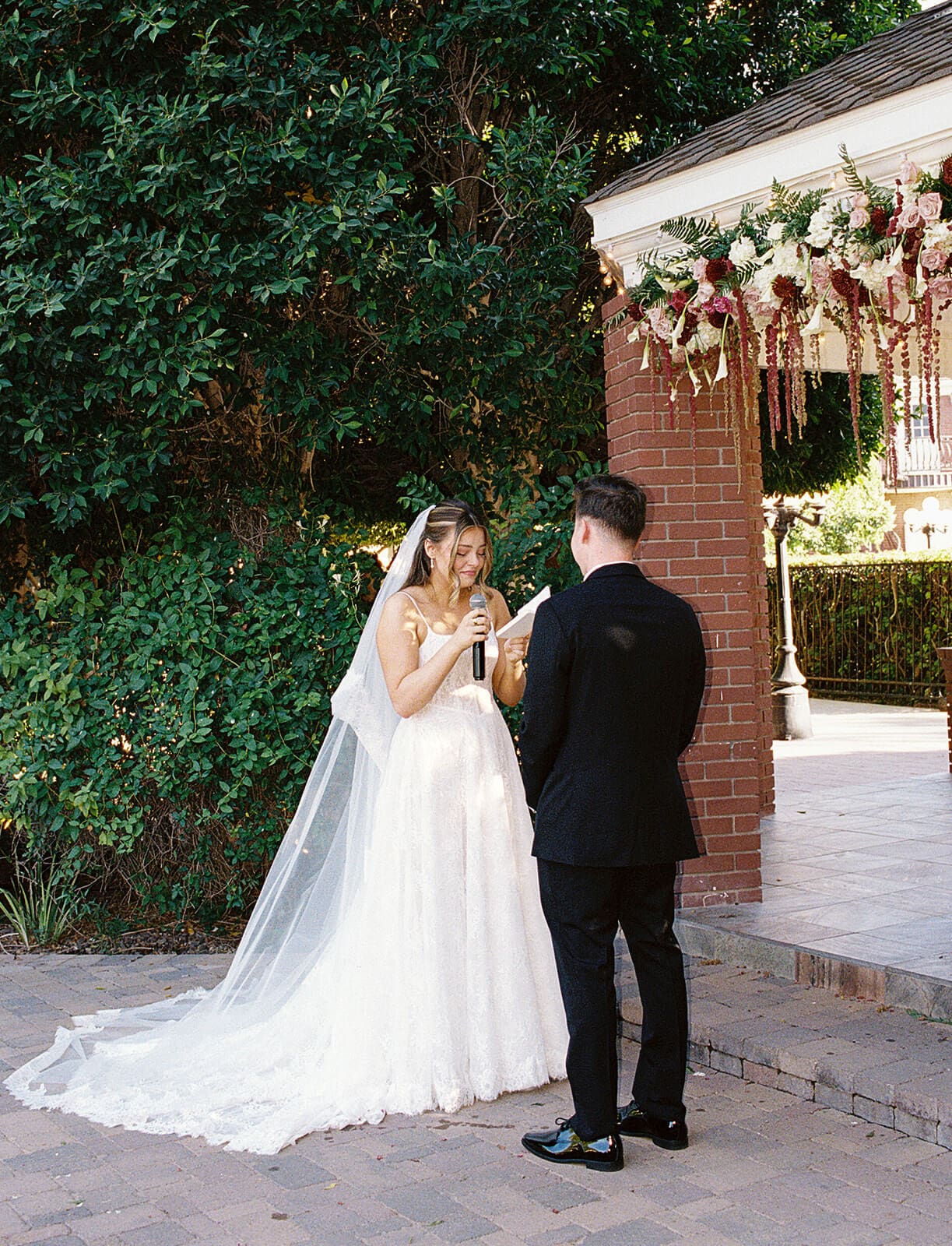 Bride and groom exchanging vows beneath the floral-covered gazebo during their outdoor ceremony at Stonebridge Manor.