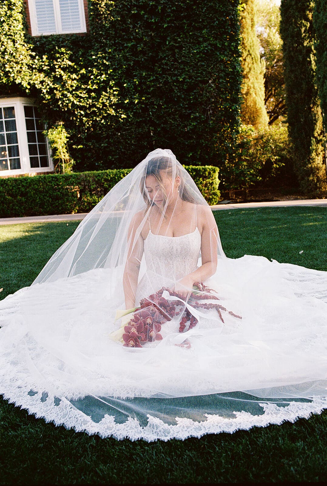 Bride sitting on her cathedral-length veil with her bouquet spread across the grass during wedding portraits at Stonebridge Manor.