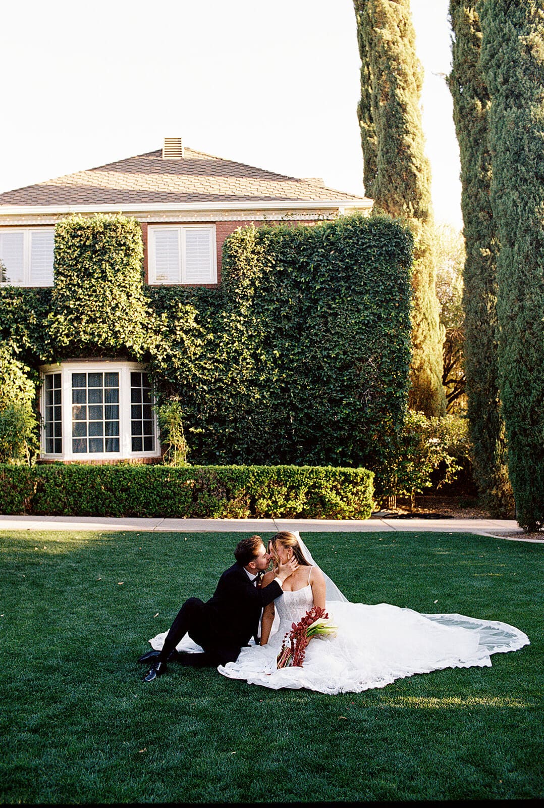 Bride and groom sitting together on the lawn in front of the ivy-covered manor house during sunset portraits at Stonebridge Manor.