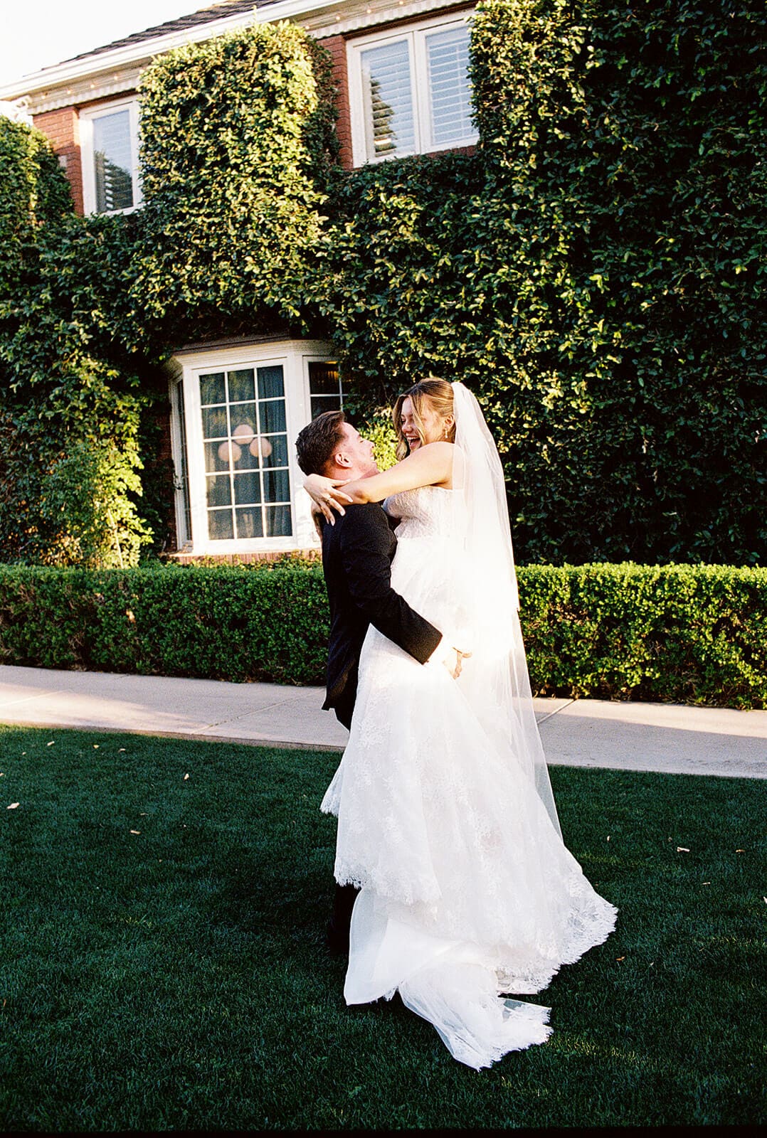 Bride jumping into the groom’s arms during sunset wedding portraits in front of the ivy-covered manor house at Stonebridge Manor.
