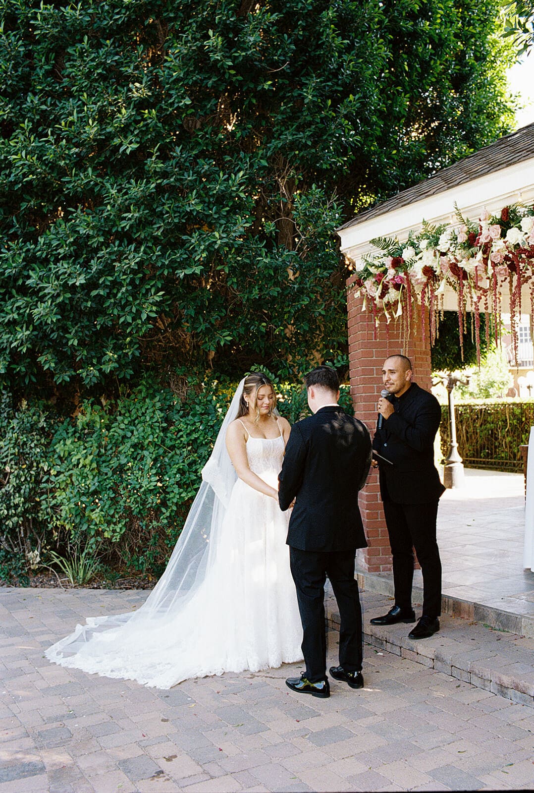 Bride and groom exchanging vows in front of the brick gazebo at Stonebridge Manor garden wedding venue in Mesa Arizona
