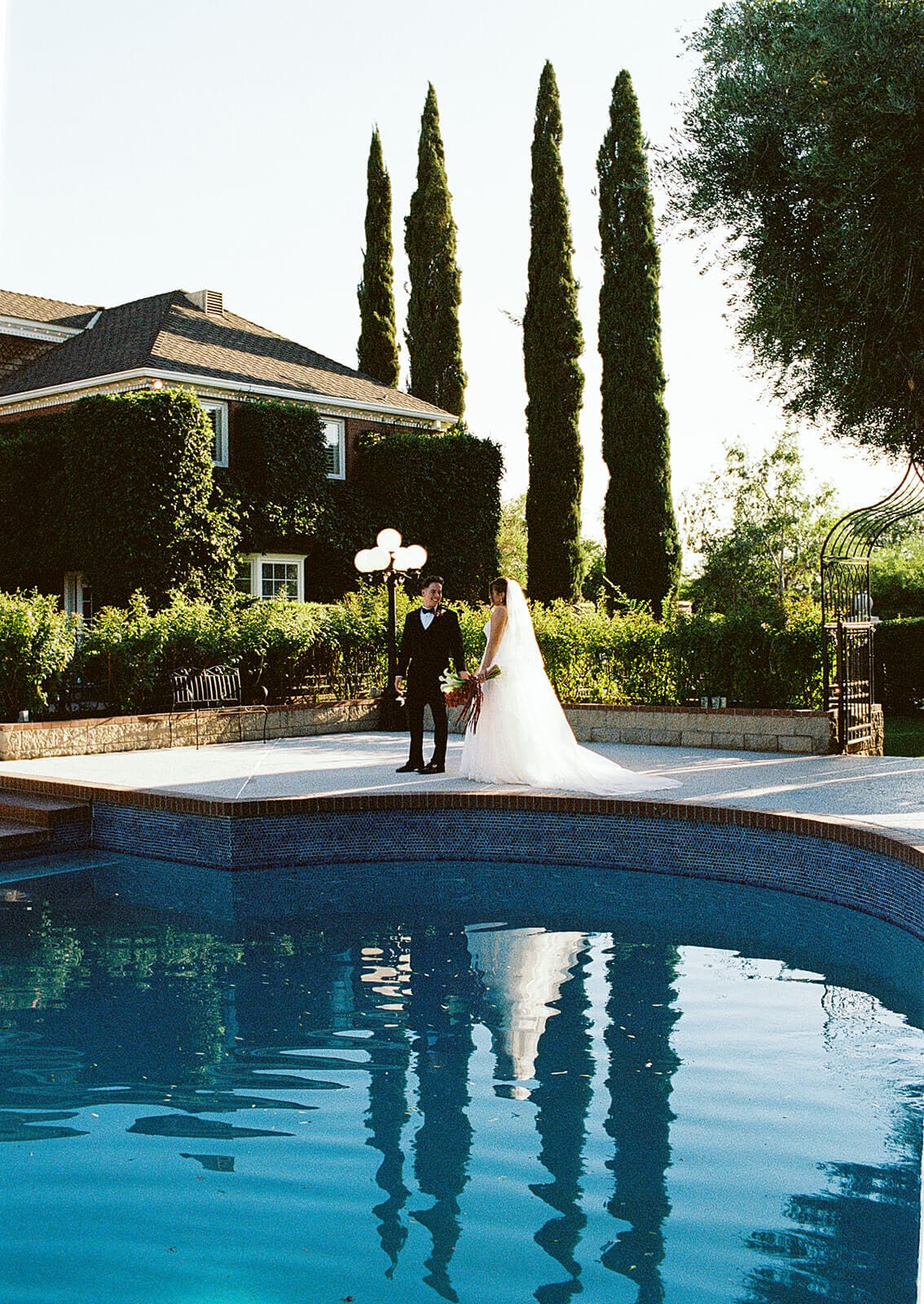 Bride and groom standing apart facing each other reflected in the blue tiled pool at Stonebridge Manor, an elegant garden wedding venue in Mesa Arizona
