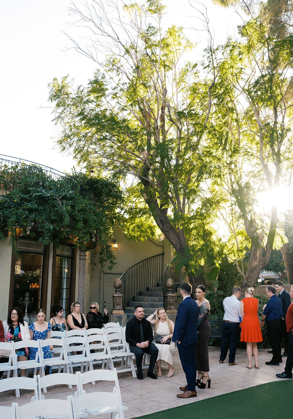 Guests mingling outdoors in the garden courtyard with sunlight filtering through the trees at Stonebridge Manor garden wedding venue in Mesa Arizona
