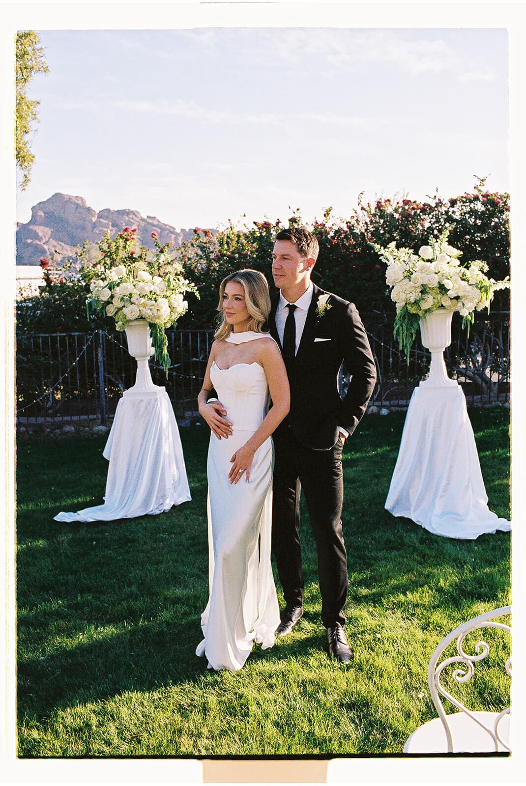 Bride and groom standing together during their outdoor Airbnb wedding ceremony with mountain views and white floral arrangements.