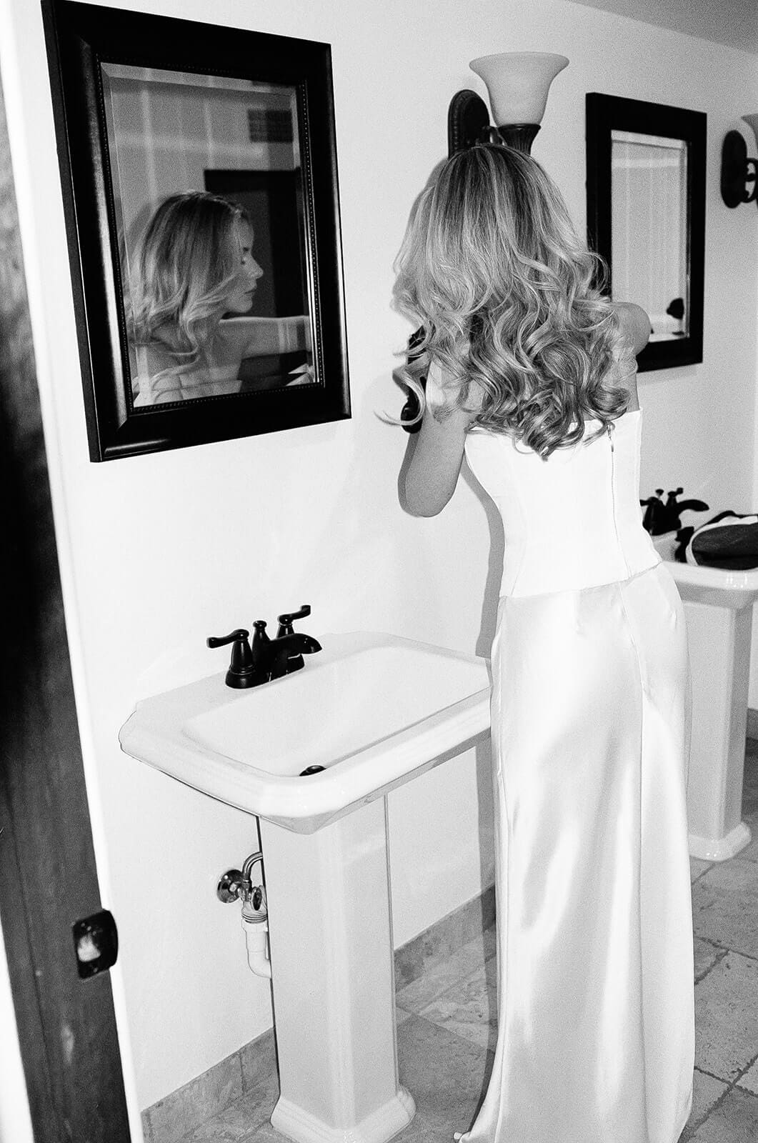 Bride checking her reflection in a bathroom mirror before her Airbnb wedding ceremony.