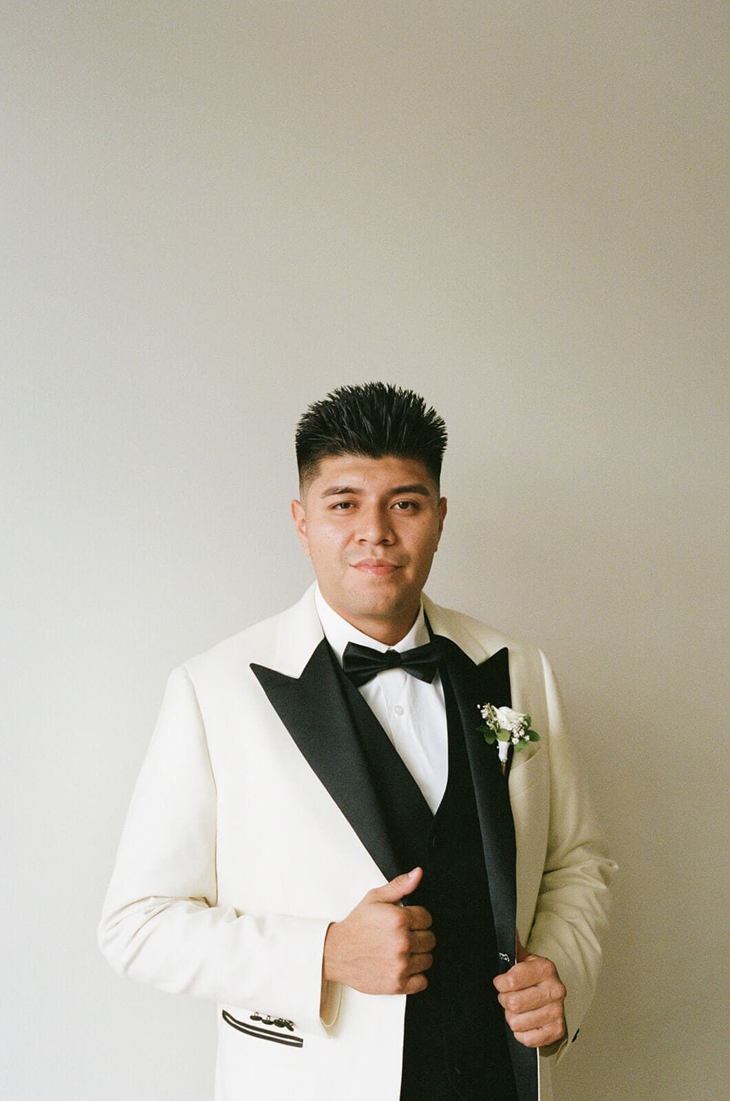 Groom wearing a white tuxedo jacket and black bow tie during his wedding-day portrait.