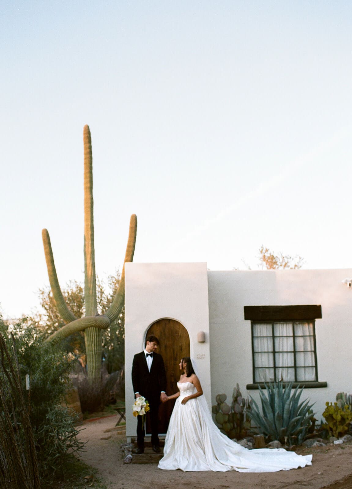 Bride and groom posing outside a desert Airbnb wedding venue with a tall cactus and Southwestern architecture.