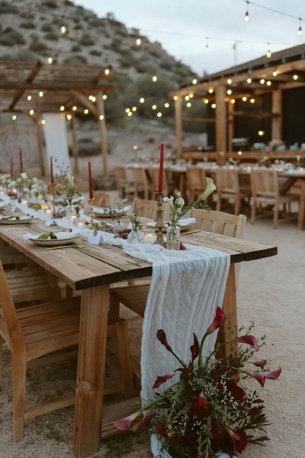 Long wooden reception tables styled with candles, florals, and string lights for a desert Airbnb wedding-style dinner at Tierra del Sol.