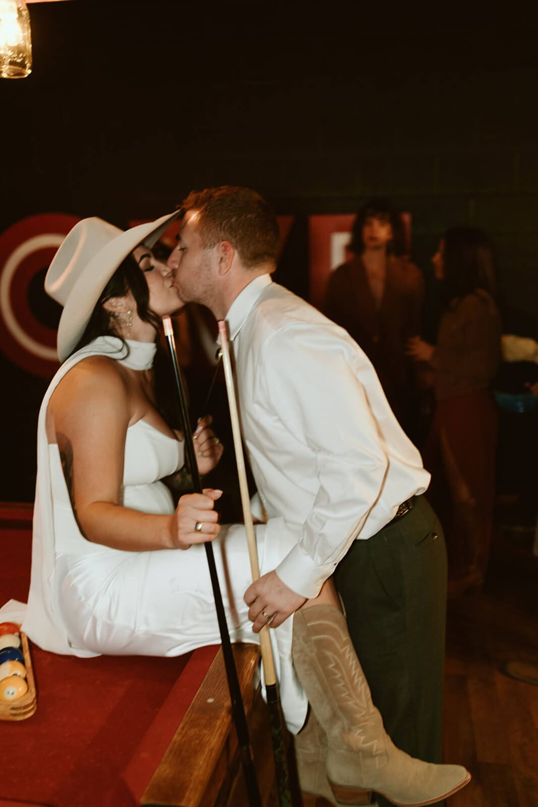 Bride and groom kissing over a pool table during their laid-back desert wedding reception.