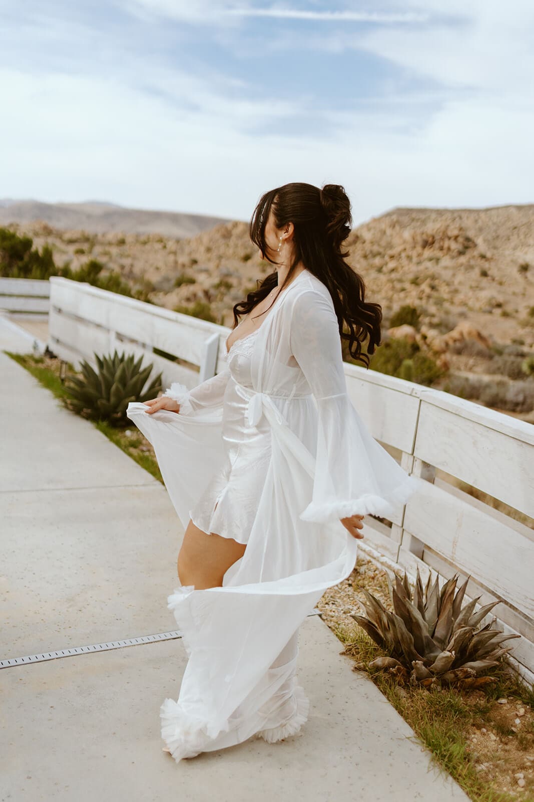 Bride walking outside in a flowing white robe with desert hills behind her before the wedding.