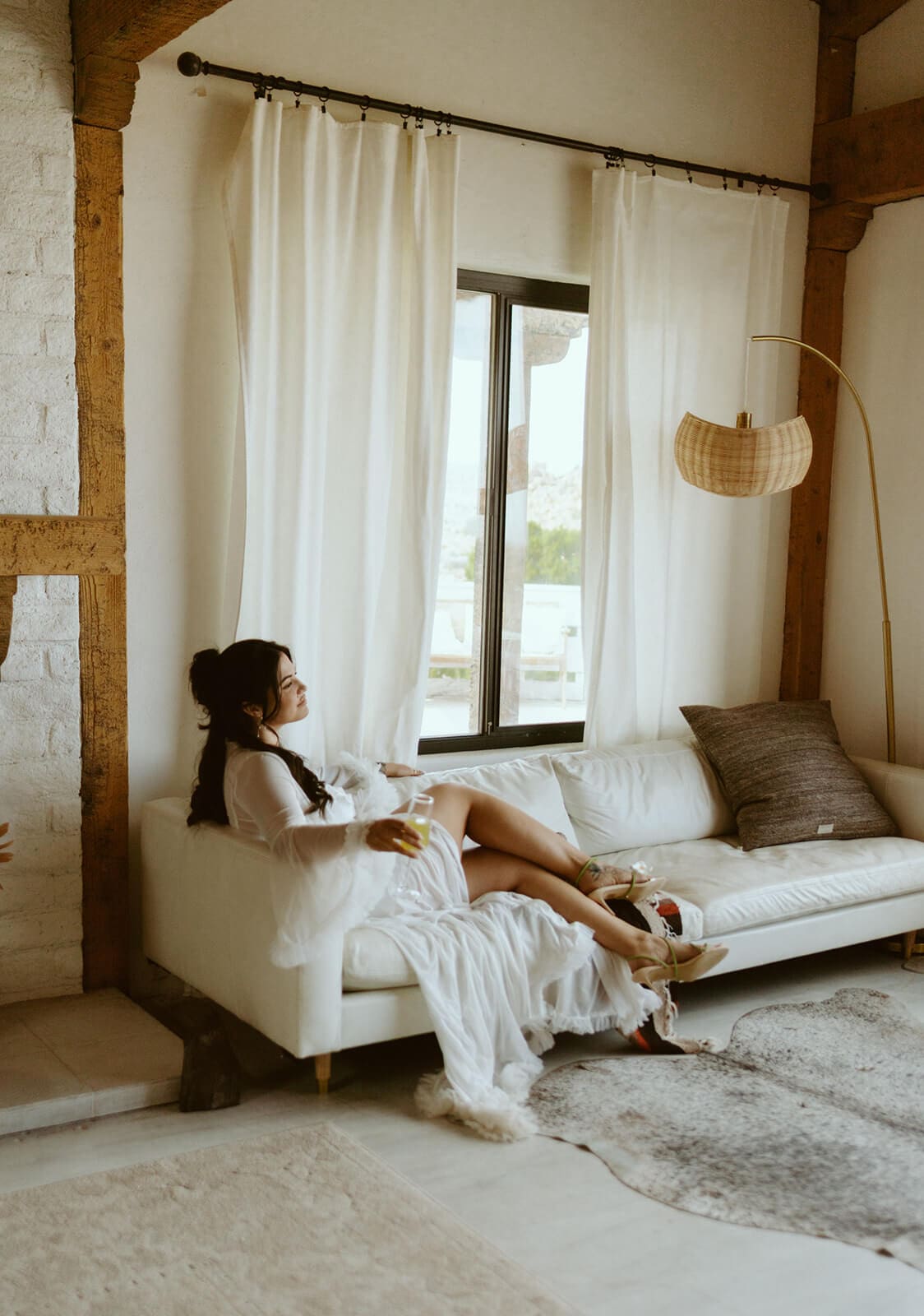 Bride relaxing on a white couch in her robe before her desert Airbnb wedding.