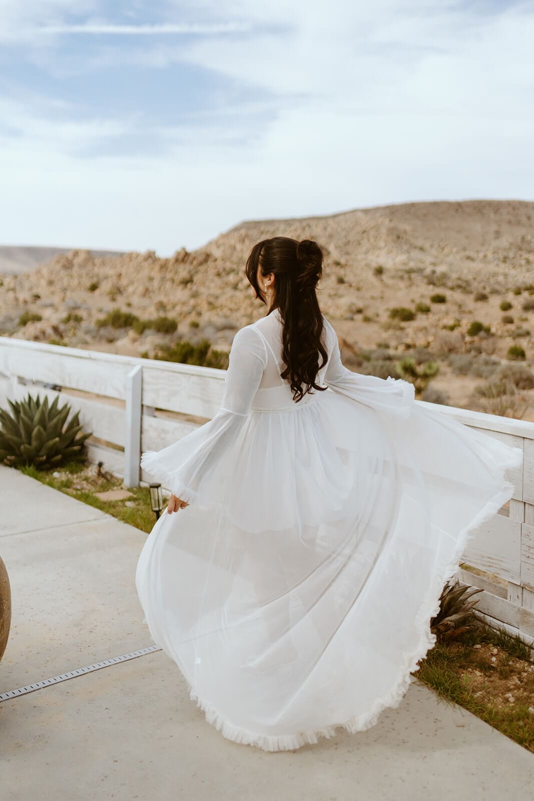Bride twirling in a sheer white robe outside an Airbnb wedding property in the desert.