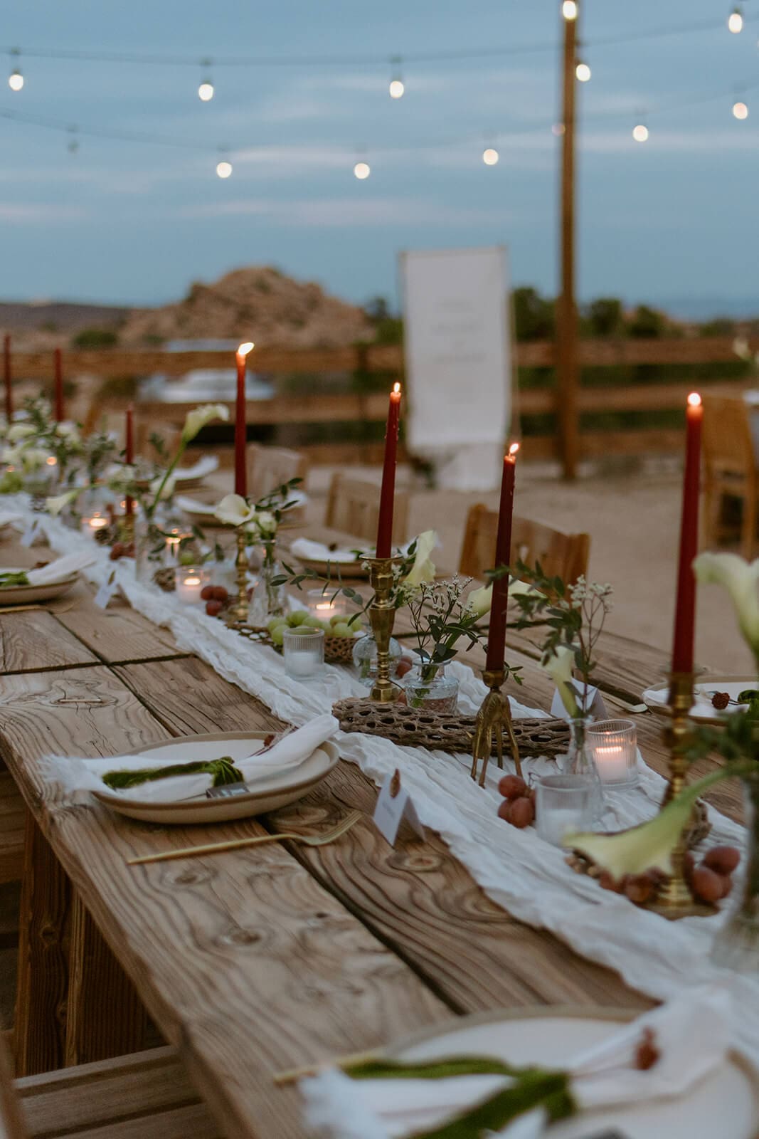 Outdoor Airbnb wedding reception table with candles, greenery, and desert views at dusk.