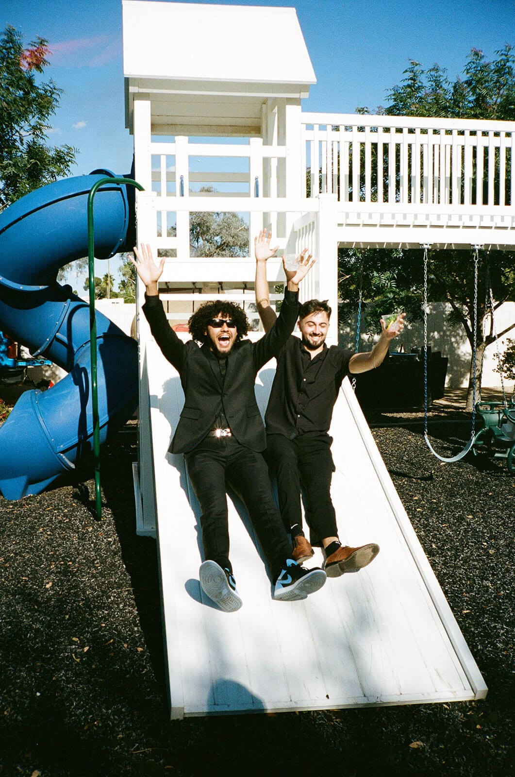 Two wedding guests sliding down a playground slide during a relaxed Airbnb wedding weekend.