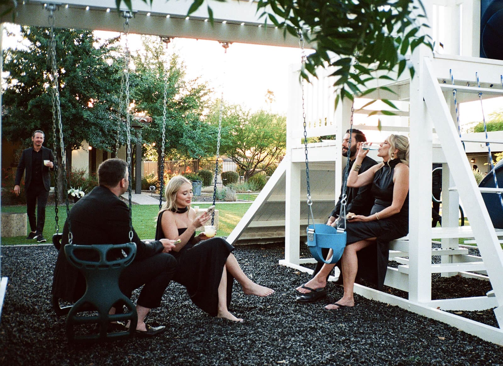 Guests sitting on swings with drinks during a casual backyard Airbnb wedding celebration.