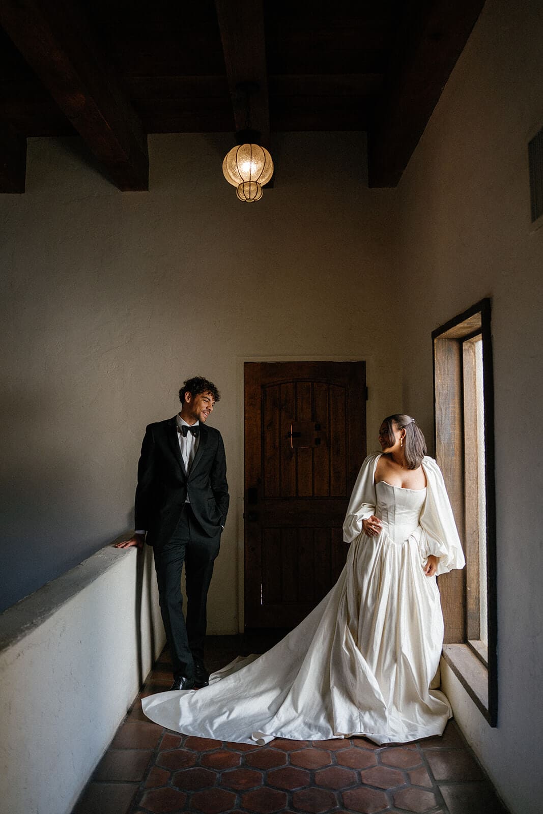 Bride and groom posing inside a moody Southwestern Airbnb wedding venue with tile floors, wooden beams, and soft window light.