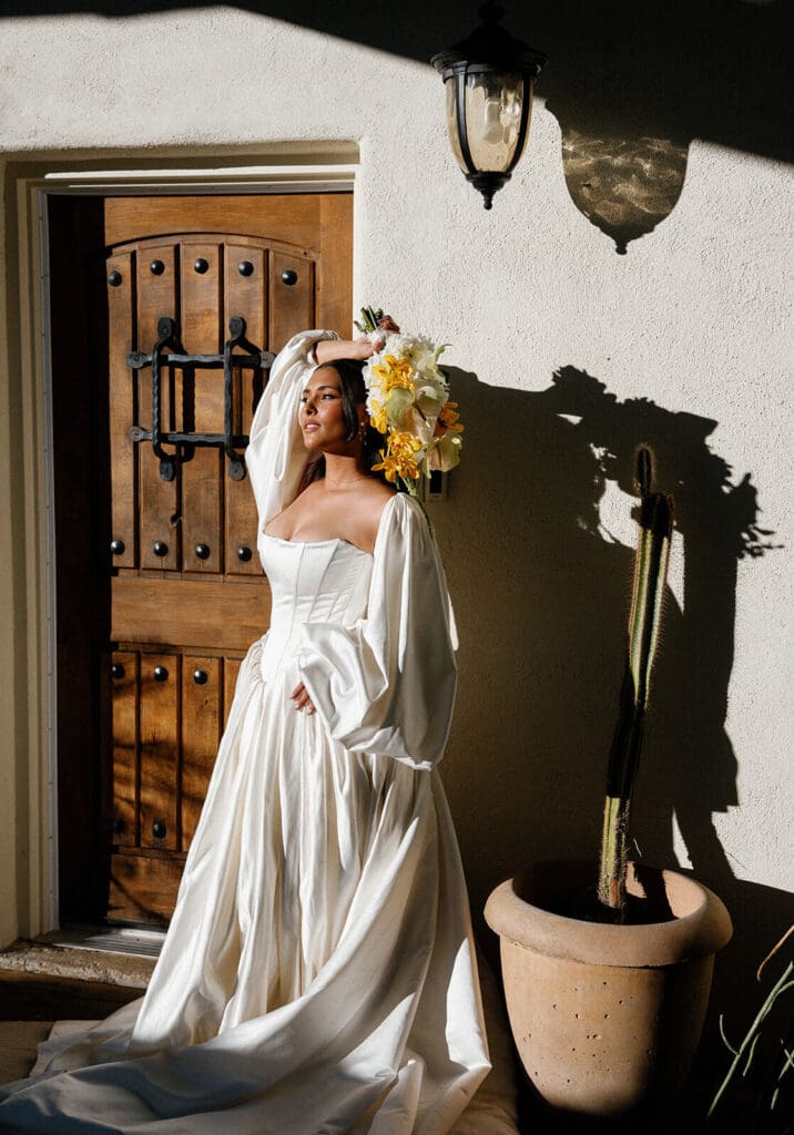 Bride posing in front of a wooden door with desert plants and bold shadows at Joshua Tree House in Tucson.