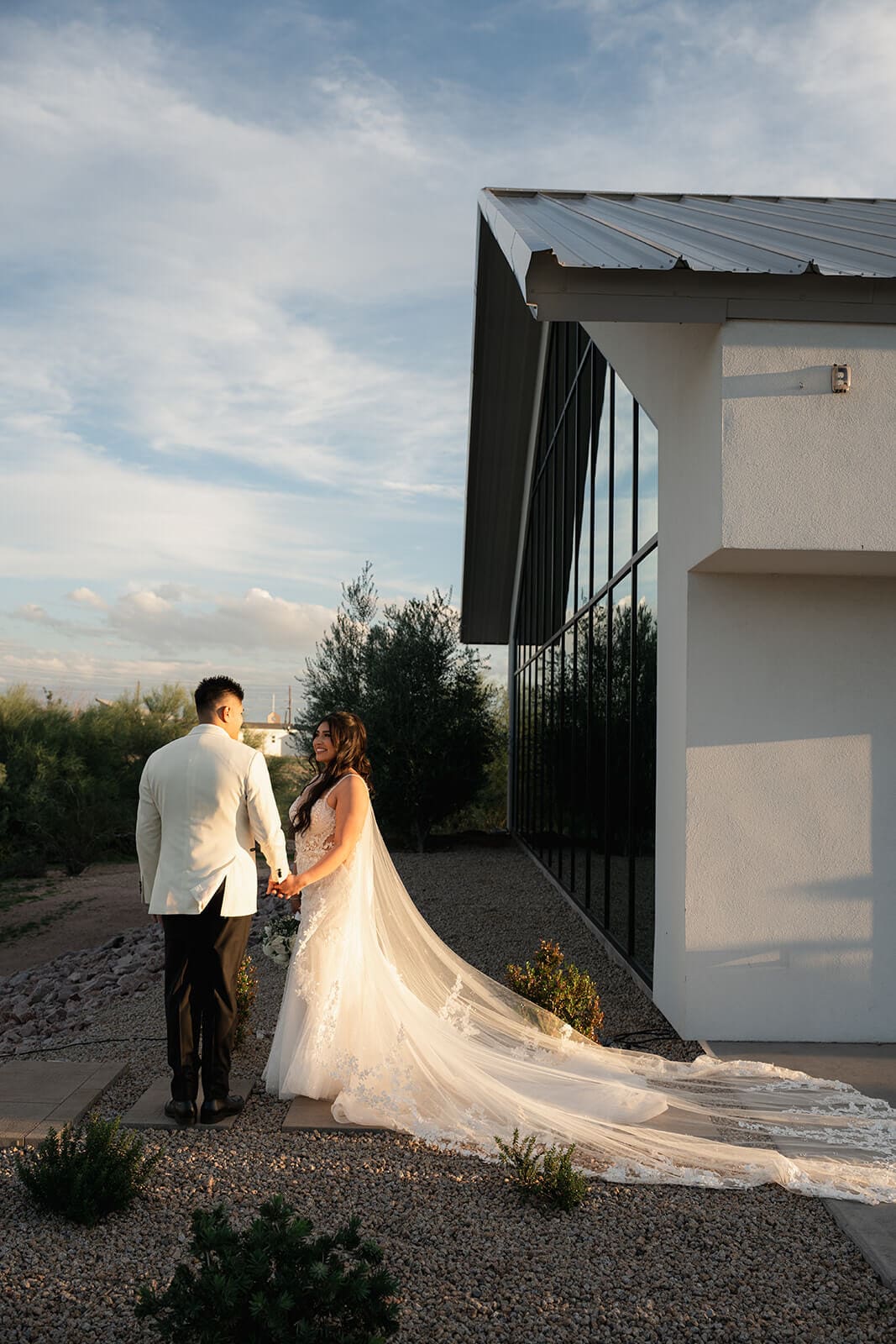 Newlyweds walking beside a modern desert wedding venue at sunset.