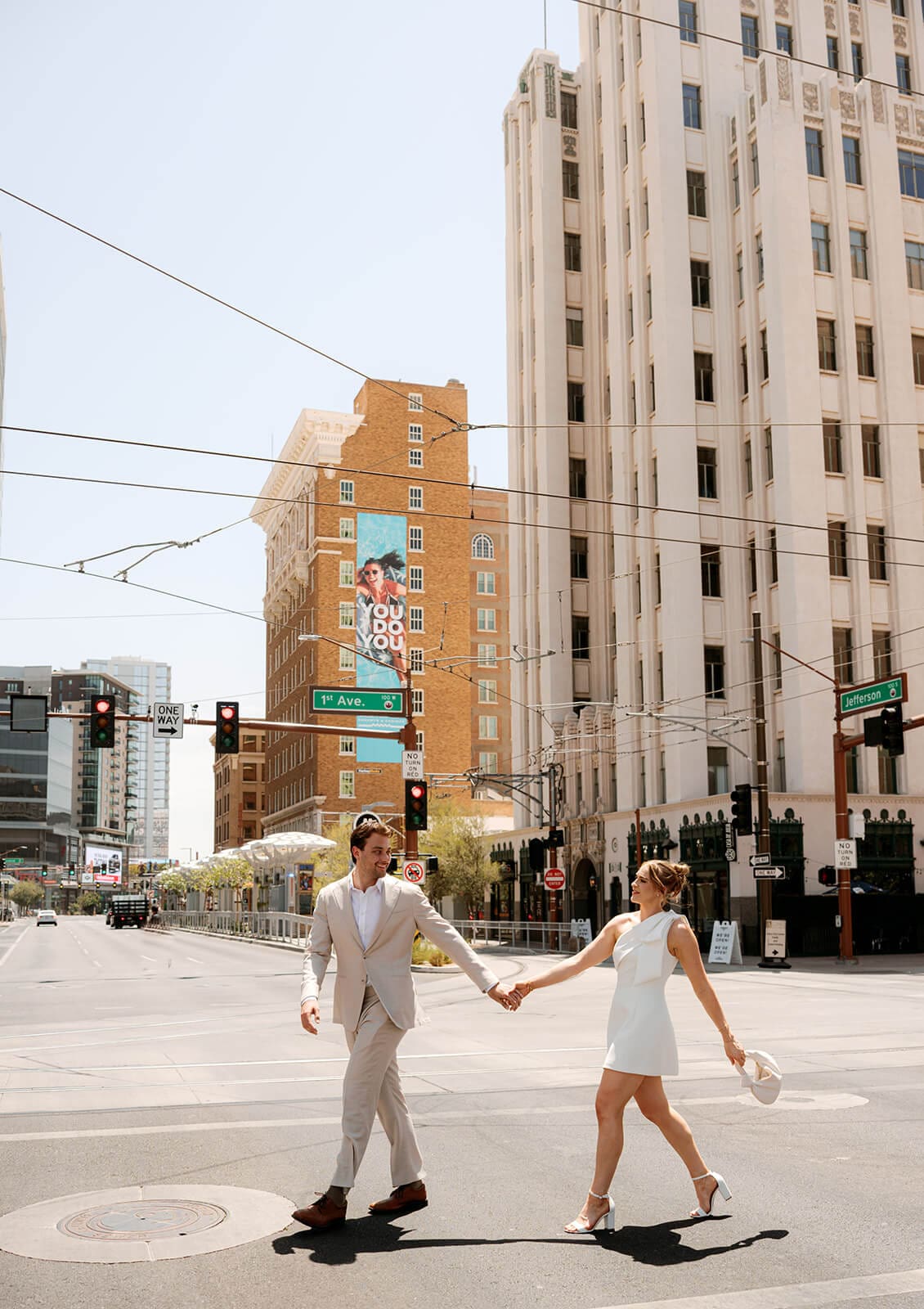 Newlyweds holding hands while crossing a downtown street surrounded by tall buildings.