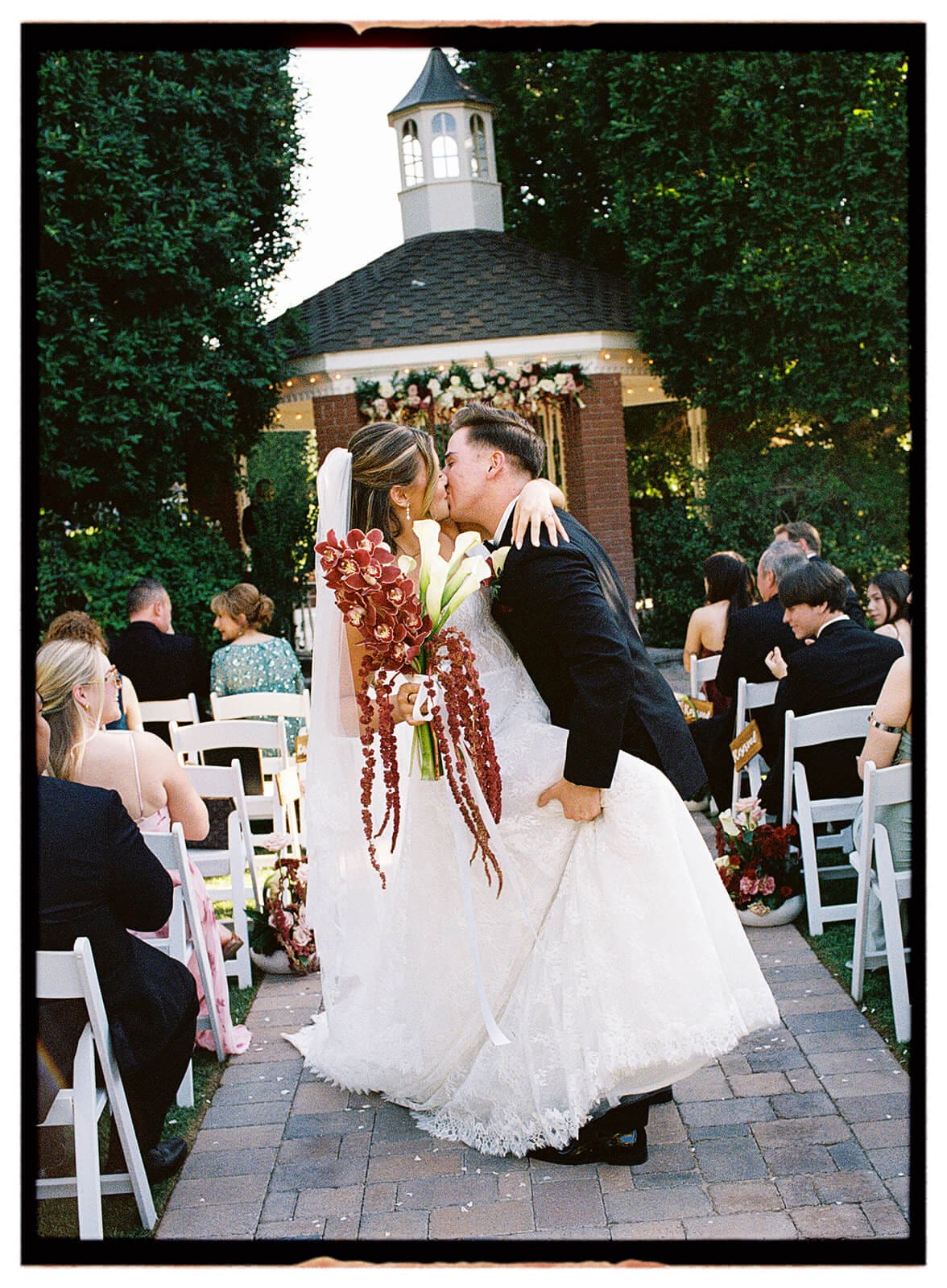 Newlyweds kissing after their outdoor wedding ceremony beneath a white cupola.
