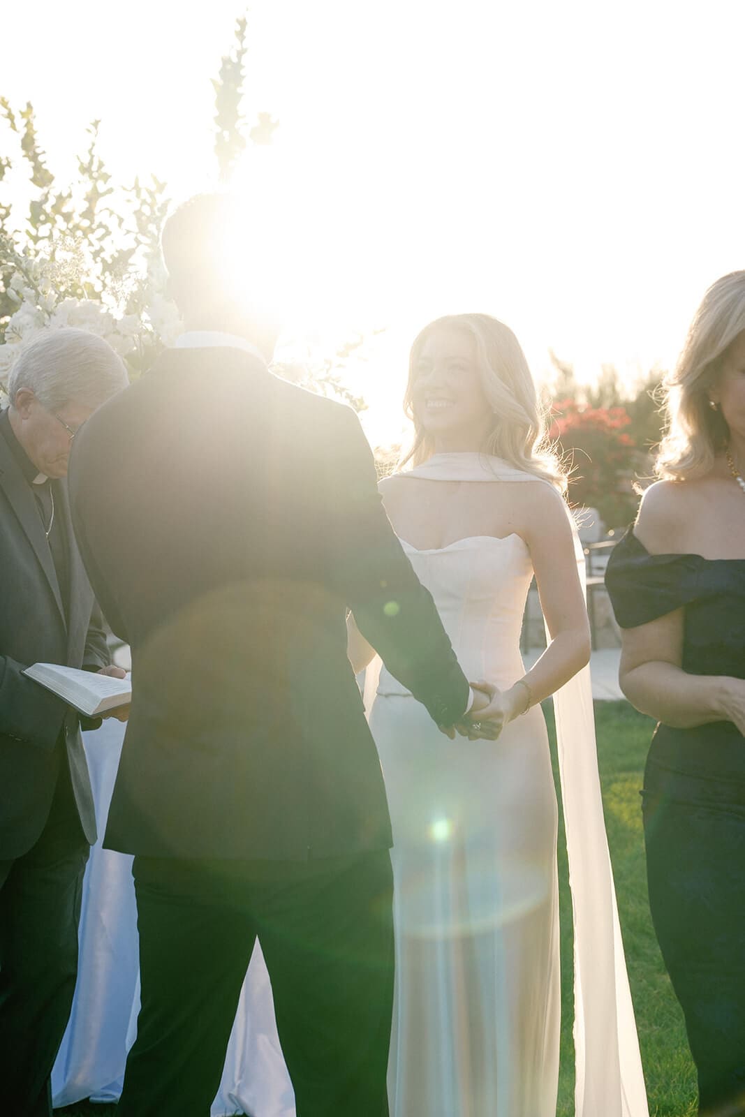 Bride walking down the aisle during an outdoor wedding ceremony in bright sunlight.
