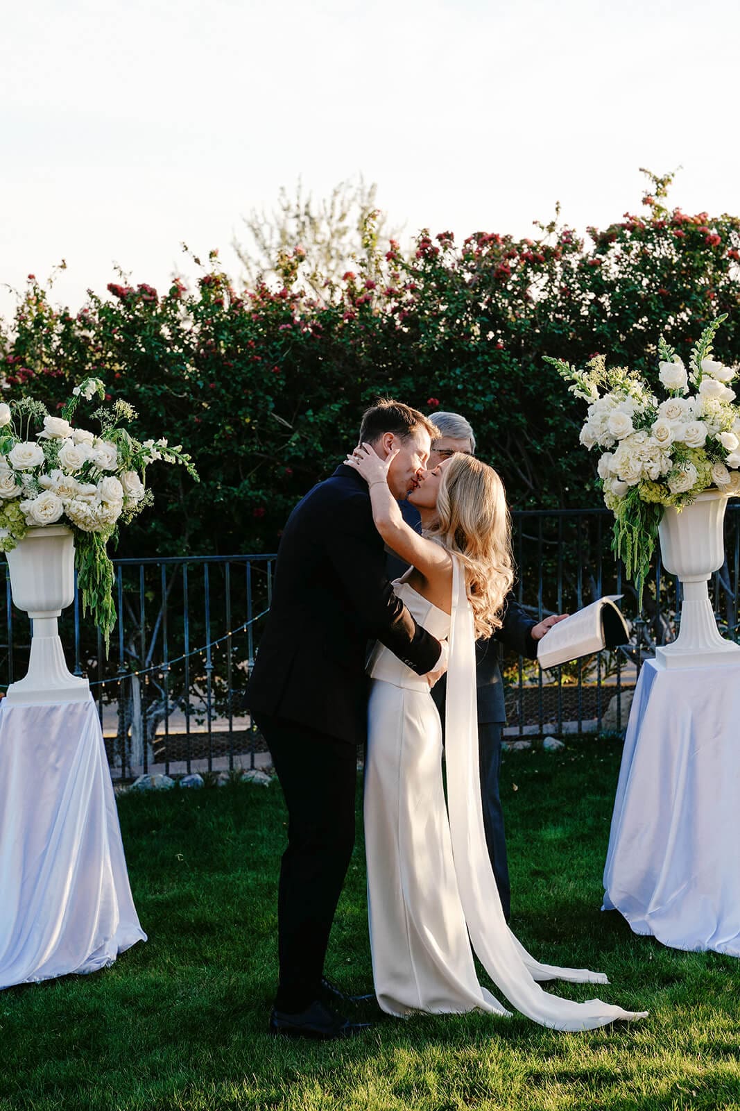 Bride and groom kissing beneath a floral ceremony arch after exchanging vows.